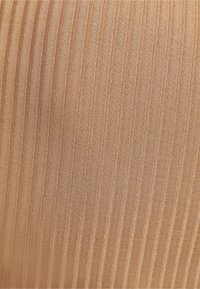 Närbild av texturerad tyg med vertikalt ribbat mönster i ljusbruna och beige nyanser.