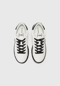 Witte sneakers met zwarte accenten, voorzien van een gladde leren bovenkant, ronde neus, zwarte veters en een stevige zwarte rubberen zool.
