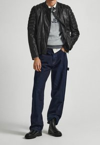 Svart läderjacka med ruggad axeldetalj, grå sweatshirt med "JEAN"-text, mörkblå jeans och svarta ankelstövlar.