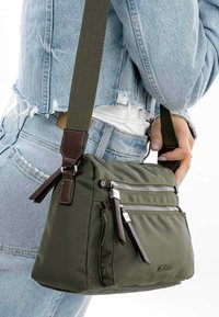 Olivengrøn nylon skuldertaske med flere lynlåslommer, brune læderdetaljer og en justerbar rem. Struktureret stof, kompakt design.