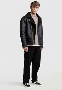 Giacca di pelle nera con colletto in shearling, maglione in cashmere beige, pantaloni neri e sneakers nere. Texture liscia, design minimalista.