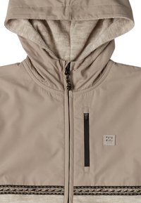 Giacca con cappuccio color beige realizzata in tessuto liscio con un morbido rivestimento in pile. Presenta una chiusura con zip frontale, tasche laterali e bordi decorativi a motivo.