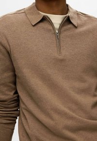 Pull col zippé marron avec un col, fabriqué en tissu tricot doux. Il présente des manches longues et une coupe décontractée avec un minimum de détails.