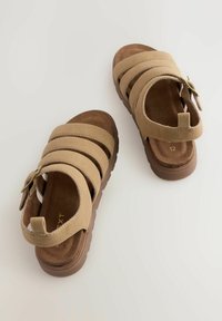 Tan-farbene Wildledersandalen mit vier breiten Riemen, einer gepolsterten Innensohle und einer strukturierten Gummisohle. Mit einem Rückriemen für einen sicheren Halt.