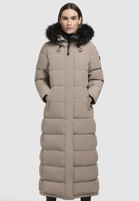 Beige párnázott hosszú kabát, szőrmebéléses kapucnival, oldalzsebekkel és elülső cipzárral. Az anyaga sima és vízálló.