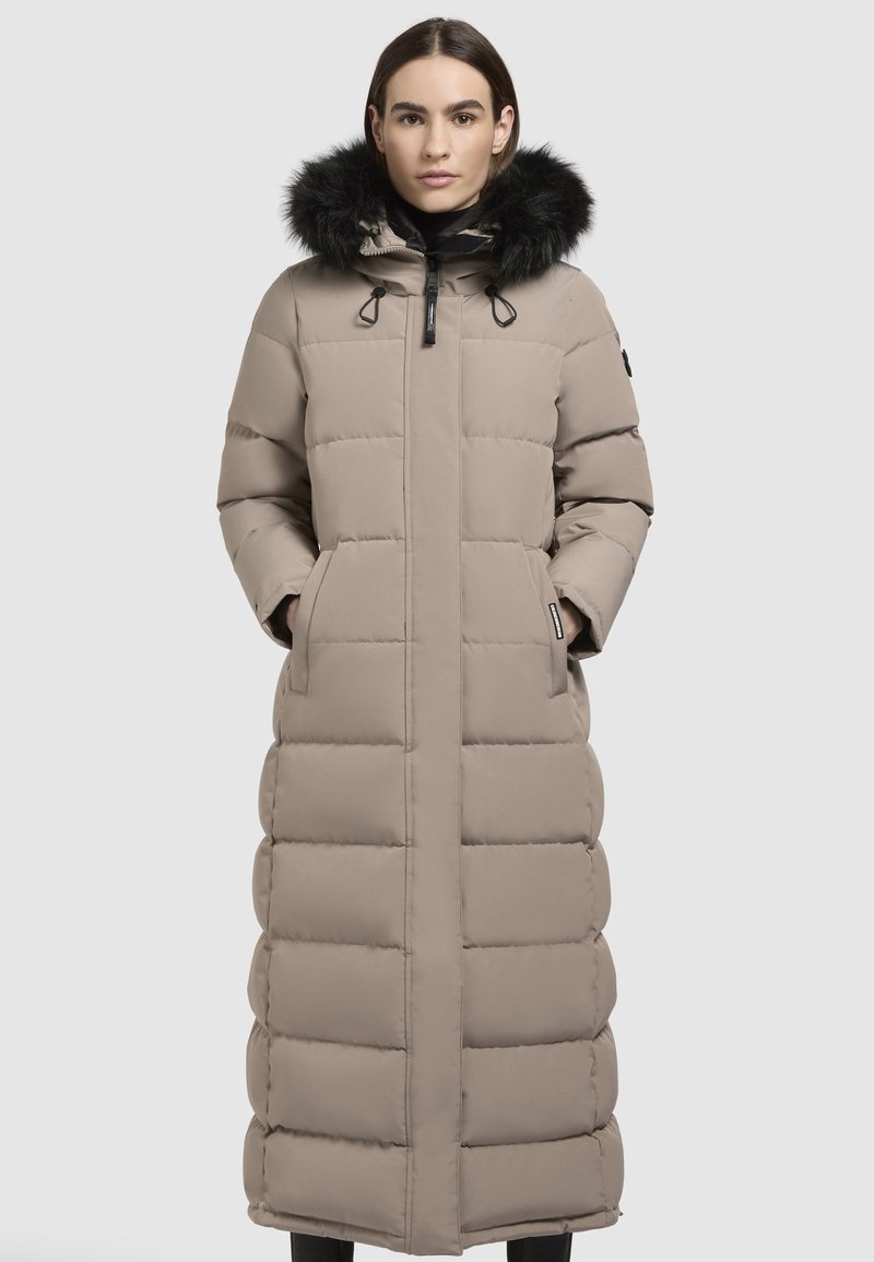 Beige párnázott hosszú kabát, szőrmebéléses kapucnival, oldalzsebekkel és elülső cipzárral. Az anyaga sima és vízálló.