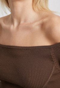 Ruskea raidoitettu olka-olka yi toppi, jossa on tekstuuri- ja leveä kaula-aukko, tiukasti istuva malli ja hienovaraiset ompelu yksityiskohdat.