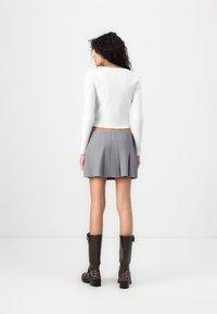 White ribbed long-sleeve top and gray pleated mini skirt, paired with knee-high brown leather boots featuring buckle details.