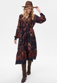 Długa, ciemna sukienka w kwiaty z taliowanym pasem i falbanowym dołem. Wykonana z lekkiego materiału, w odcieniach burgundu z złotymi akcentami.