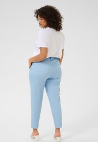 Pantalones celestes con un corte ajustado, que cuentan con bolsillos laterales y una textura suave. Combinados con una blusa blanca de manga corta.
