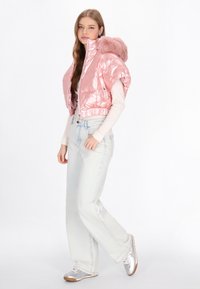 Różowa, błyszcząca kurtka puchowa z kapturem ozdobionym sztucznym futrem, krótki fason, skomponowana z jasnoniebieskimi, luźnymi dżinsami i srebrnymi trampkami.