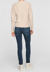 Béžový žebrovaný svetr s uvolněným střihem, kombinovaný s tmavě modrými skinny džíny a smetanovými kotníkovými botami s texturovanou podrážkou.