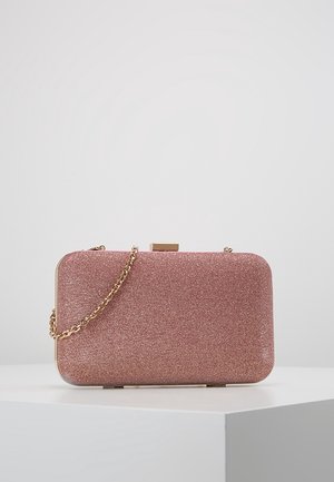 Bolso de mano rectangular rosa brillante con cadena dorada y cierre dorado, colocado sobre una superficie blanca contra un fondo liso.