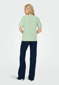 Lys grøn t-shirt med korte ærmer, afslappet pasform, parret med mørkeblå flagrende jeans, glat tekstur, synlige syninger på denim.