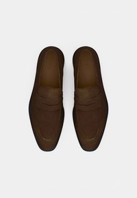 Καφέ μοκασίνια από σουέτ με λεία υφή, που διαθέτουν ραμμένη λεπτομέρεια και αντίθετη μαύρη λαστιχένια σόλα. Σχεδιασμός τύπου παντοφλών, με ανοιχτή φτέρνα.