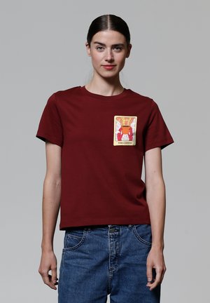 T-shirt bourgogne à manches courtes avec un graphique carré représentant un pot et le texte "LE CAFÉ" sur un fond crème.
