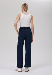 Mörkblå vida jeans med hög midja, med uppvikta fållar, en bakficka och en slät textur, kombinerade med en vit linne.