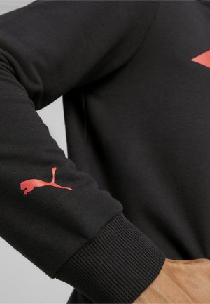 Czarny sweatshirt z prążkowymi mankietami; posiada czerwone logo Pumy na lewym rękawie; gładka tekstura i swobodny fason.