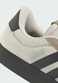 Adidas tenisica s teksturiranim gornjim dijelom od bež tkanine, smeđim kožnim detaljima i crnim gumiranim potplatom s tri tamna pruga.