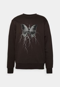 Sudadera negra con un gráfico de mariposa y diseño de relámpagos. Los materiales parecen suaves; los puños y dobladillo acanalados proporcionan un ajuste estructurado.