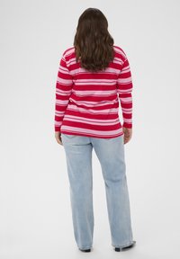 Czerwono-różowa bluzka w paski z długim rękawem o luźnym kroju, zestawiona z jasno-niebieskimi dżinsami, widoczna długość i proste wykończenie przy kostkach.