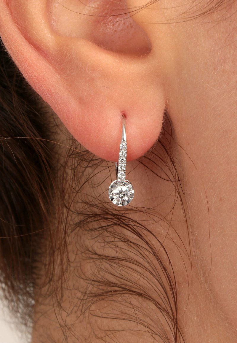 Nahaufnahme eines Ohrläppchens mit einem silbernen Tropfenohrring, der eine Reihe kleiner Diamanten und einen größeren runden Diamanten am Ende hat.