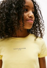 Żółta bawełniana koszulka z okrągłym dekoltem i krótkimi rękawami, z nadrukowanym logo "TOMMY HILFIGER EST. 1985" na środku.