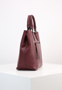Bordeaux leren handtas met dubbele handvatten, zijrits zak en gestructureerde vorm. Voorzien van contrasterende zwarte stiksels. Gladde textuur.