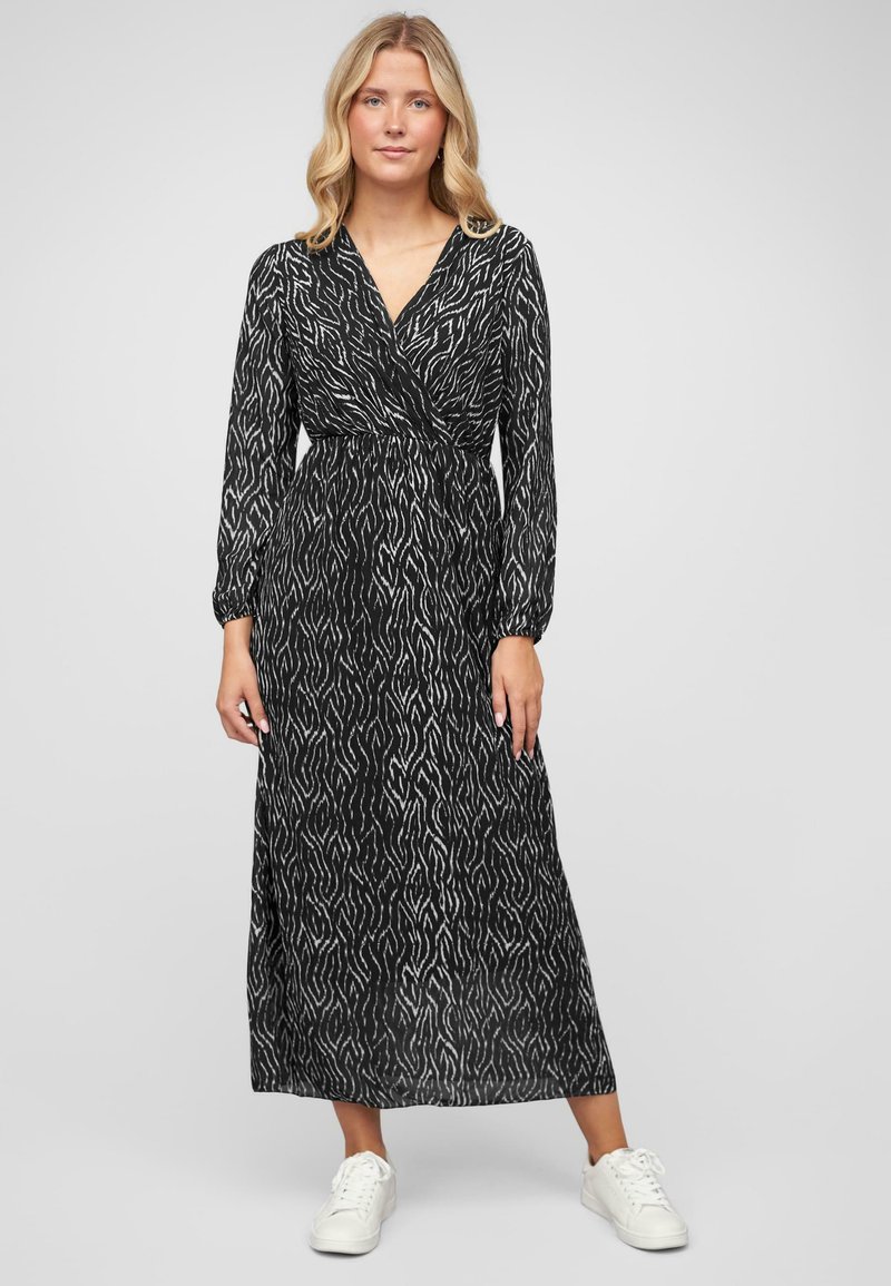 Black long-sleeve dress with white abstract pattern, wrap-style bodice, elastic waist, and flowy skirt, paired with white sneakers.