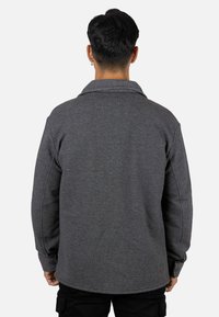 Chaqueta gris de tela texturizada, con cuello vuelto y puños abotonados, mostrada desde atrás.