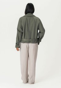 Olivengrüne Jacke mit lässiger Passform, großem Kragen und verstellbaren Bündchen, kombiniert mit hellgrauen, locker sitzenden Hosen.