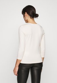 Ljusbeige långärmad skjorta med rund halsringning, figurnära design och mjukt material, kombinerad med svarta läderbyxor.