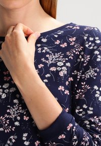 Camiseta de manga larga en color marino con estampado floral en rosa y blanco, que presenta un cuello redondo y puños acanalados. Se puede apreciar la suavidad de la textura de la tela.