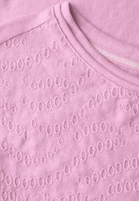 Tissu en coton rose clair avec des motifs circulaires texturés ; encolure lisse avec une finition côtelée et un subtil rayé horizontal.