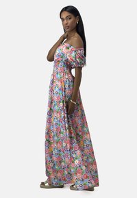 Robe maxi fleurie avec des manches dénudées, ornée de fleurs roses, rouges et violettes sur fond bleu clair, avec un buste smocké et une longue jupe.