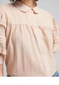 Blusa corta a maniche corte color rosa chiaro con design arricciato, sottili righe verticali e chiusura a bottoni. Tessuto morbido con colletto.