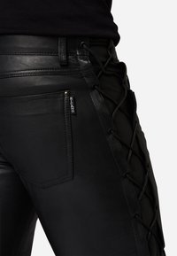 Schwarze Lederhosen zeichnen sich durch ein eng anliegendes Design mit Schnürdetails an der Seite, einer Metall-Reißverschlusstasche und einem dezenten Branding-Tag aus.