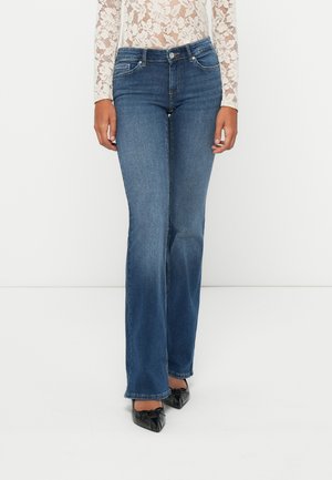 Blaue Jeans im Schlagstil aus Denim mit mittelhohem Bund, ausgestattet mit fünf Taschen und subtiler Ausbleichung entlang der Beine. Getragen mit schwarzen, spitzen Ballerinas.