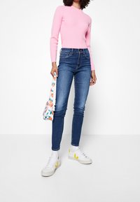 Suéter rosa ajustado de canalé, jeans oscuros de tiro alto, zapatillas blancas con detalles amarillos y un bolso cruzado floral.