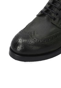 Zwarte leren brogue schoen met perforatie-details, ronde neus en veters. Heeft een gladde afwerking en een contrasterende zwarte zool.