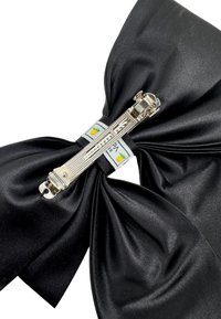 Black satin bow with a central silver clip. Features a textured surface and two small labels with a fruit design.
