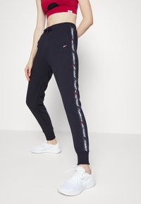 Schwarze Sweatpants mit einem figurbetonten Design, verziert mit weißem Branding an der Seite, mit gerippten Knöcheln und einem verstellbaren Kordelzugbund.