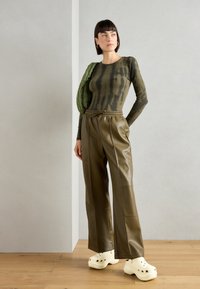 Top verde a maniche lunghe con effetto tie-dye, pantaloni a gamba larga in ecopelle oliva e zoccoli bianchi. L'outfit è completato da una borsa verde trapuntata.