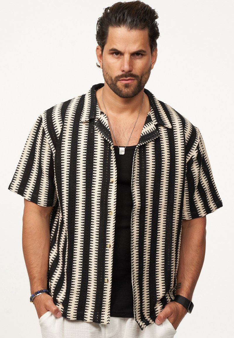Kurzarmhemd mit einem geometrischen Muster aus schwarz-beigen Streifen, Knopfleiste und leichtem Stoff. Auffällige strukturierte Details sind enthalten.