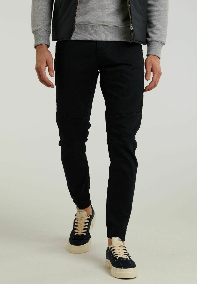 Pantalones negros ajustados con detalles de panel, hechos de una tela suave. Combinados con zapatillas navy con suela y cordones crema.