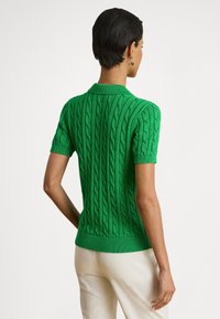 Grønn kortermet polo-genser med kabelstrikket tekstur, ribbestrikket krage og kant. Laget av et elastisk strikket materiale.