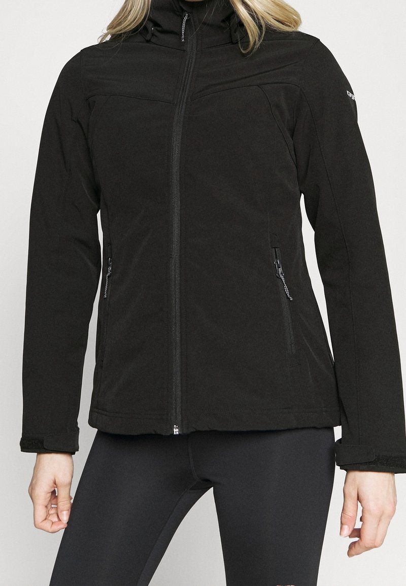 Femme portant une veste noire ajustée à fermeture éclair avec des poches latérales zippées et des manches longues, assortie à un legging noir.