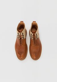 Bruine leren enkelboots met een tan kleurige bovenkant, voorzien van ronde veters, contrasterende stiksels en een ronde neus. Opvallende textuurdetail.