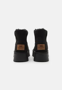 Stivaletti neri in suede con una morbida fodera in pelliccia, una toppa in pelle marrone con logo sul retro e una suola in gomma spessa.