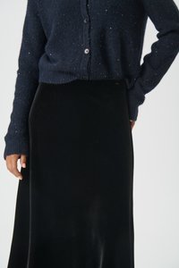 Mornarsko pleteno kardigan s sijajnimi podrobnostmi, z gumbi; kombiniran z črno žametno maksi krilo, gladke teksture in elegantne silhuete.
